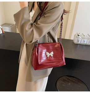 Close-up of wine red embossed leather shoulder bag with silver butterfly and chain strap
