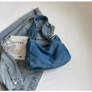 Close-up of blue denim hobo bag with side drawstring pockets on casual background