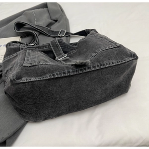 Detailed close-up of dark grey denim crossbody bag with white stitching and silver buckles