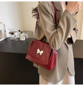 Detail of burgundy crocodile-embossed shoulder bag with a silver butterfly metal clasp