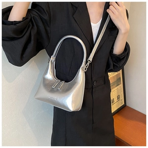 Model wearing a silver metallic crescent bag with an adjustable shoulder strap and handle