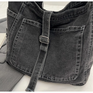 Detail of dark washed denim shoulder bag showing white contrast stitching and pocket