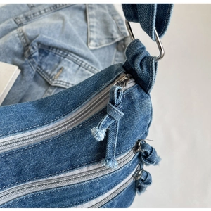 Detailed close-up of dark blue denim tote bag with layered zipper pockets and raw edge knots