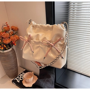Detail of creamy white patent leather bucket bag with pink bows and silver chain straps