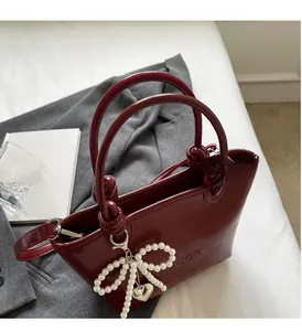 Détail du sac à main bordeaux brillant avec nœud en perles et pendentif cœur