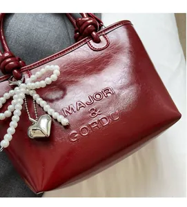 Détail du sac seau en cuir verni rouge avec lettrage gaufré et breloque perle nœud