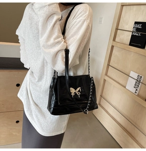 Detail of black crocodile texture shoulder bag featuring silver butterfly buckle and chain