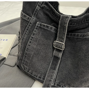 Detailed close-up of dark denim bag with contrast stitching and metal buckle strap