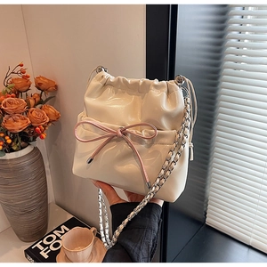 Detail of cream patent leather bucket bag featuring a soft pink bow and silver chain strap