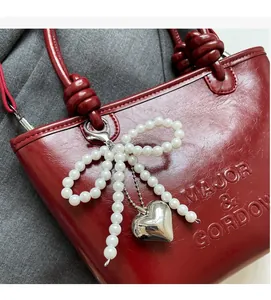 Détail du sac seau en cuir rouge avec nœud en perles et pendentif cœur en argent