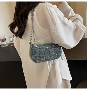 Detail of blue denim shoulder bag with rhinestones and silver chain strap on model