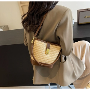 Detail der Stroh-Eimertasche mit braunem Lederbesatz und Goldverschluss am Modell