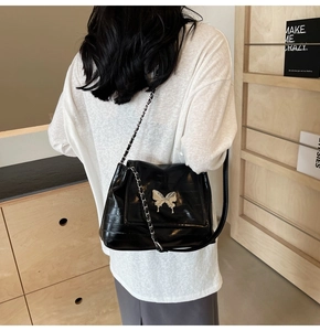 Detail of black glossy shoulder bag with silver butterfly buckle and chain strap on model