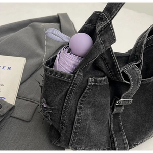 Detail view of denim crossbody bag with white stitching and frayed pocket for umbrella