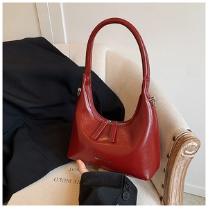 Detailed close-up of crescent underarm bag in glossy burgundy with metal zippers