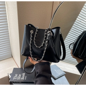 Detail of glossy black patent leather bucket bag with silver chain and adjustable strap