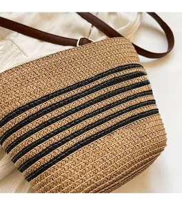 Close-up of woven straw shoulder bag featuring black stripes and adjustable leather strap