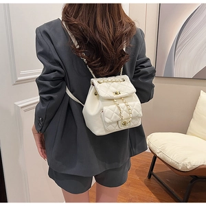 Detail of a white quilted mini backpack with gold chain straps worn by a model
