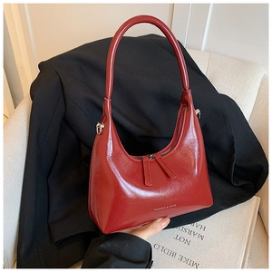 Close-up of red patent leather hobo bag with dual zippers and decorative logo text