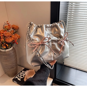 Close-up of silver bucket bag featuring pink bow accent and metal chain strap details