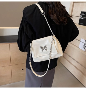Close-up of white embossed tote bag with silver butterfly charm and chain strap detail