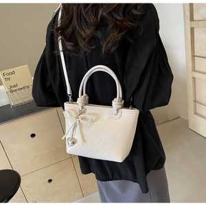 Détail du sac seau en cuir PU crème avec lettres gaufrées et charm nœud en perles