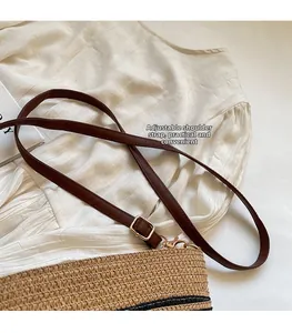 Detail of adjustable leather shoulder strap with gold buckle on woven straw bucket bag