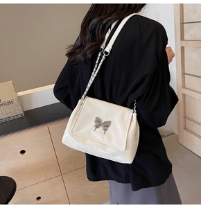 Close-up of cream white shoulder bag with silver butterfly buckle and chain strap detail