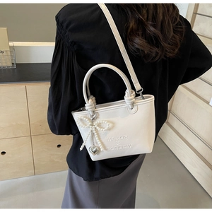 Détail du sac seau en cuir blanc avec logo embossé et pendentif nœud en perles