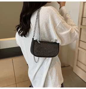 Detail view of black handbag with silver rhinestones and chain strap worn by a model