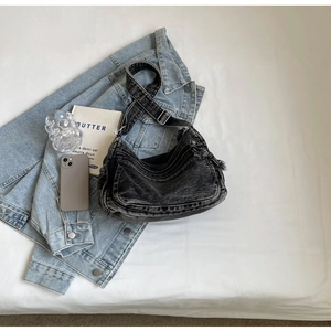 Detailed view of washed denim hobo bag with multiple zippers on white bedding background