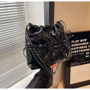Close-up of black patent leather bucket bag featuring a bow drawstring and chain strap