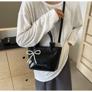 Détail du sac seau en cuir PU brillant noir avec nœud en perles et pendentif cœur