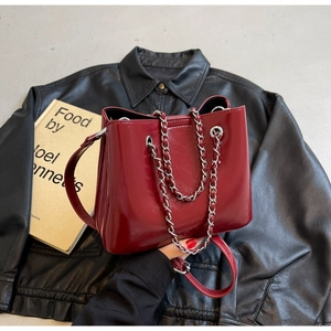 Macro view of burgundy glossy leather bucket bag with silver chain straps on black jacket