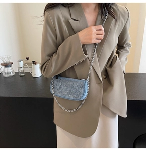 Light blue denim handbag with rhinestones worn by a model in a modern cafe setting