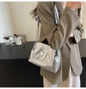 Close-up of a silver metallic tote bag featuring a decorative metal butterfly and chain