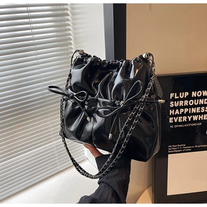 Detail of black glossy drawstring bucket bag with silver chain and bow knot detail