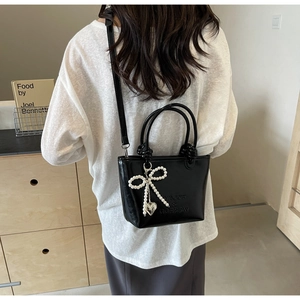 Détail du sac seau en cuir noir brillant avec pendentif perle et logo en relief