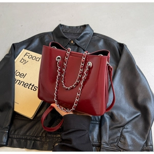Detail of burgundy patent leather bucket bag with silver chain handle and leather strap