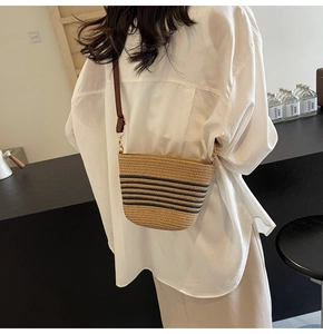 Detail of woven straw bucket bag featuring black stripes and brown leather strap