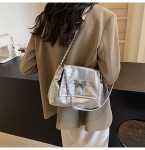 Silver chain shoulder bag with metallic butterfly buckle shown on model in cafe setting