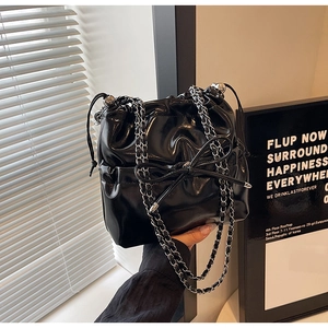 Detail of black glossy bow backpack with chain straps and drawstring bucket design