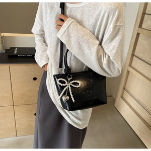 Détail du sac seau noir brillant avec nœud en perles et pendentif cœur en métal
