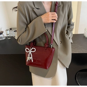 Détail du sac seau bordeaux avec nœud perlé et breloque cœur sur blazer kaki