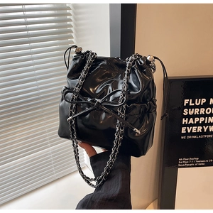 Detail of glossy black patent leather bucket bag with bow and silver chain strap