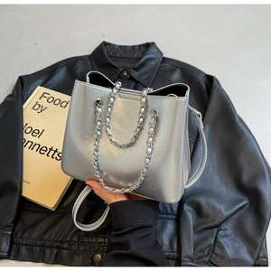 Detail of silver metallic tote bag with chain handle and adjustable leather strap on black jacket