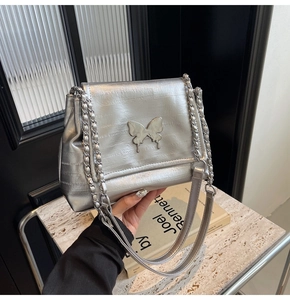 Detailed view of silver pleated shoulder bag with metallic butterfly buckle and chain strap