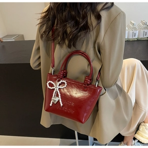 Détail du sac à main en cuir verni rouge avec nœud en perle et pendentif cœur
