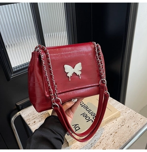 Detail of red embossed leather shoulder bag featuring a large silver butterfly buckle