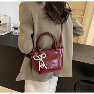 Détail d'un sac seau en cuir bordeaux avec breloque nœud de perles porté à l'épaule